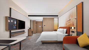 Una habitación de hotel moderna con cama, sofá, televisor, escritorio y una obra de arte grande en la pared.