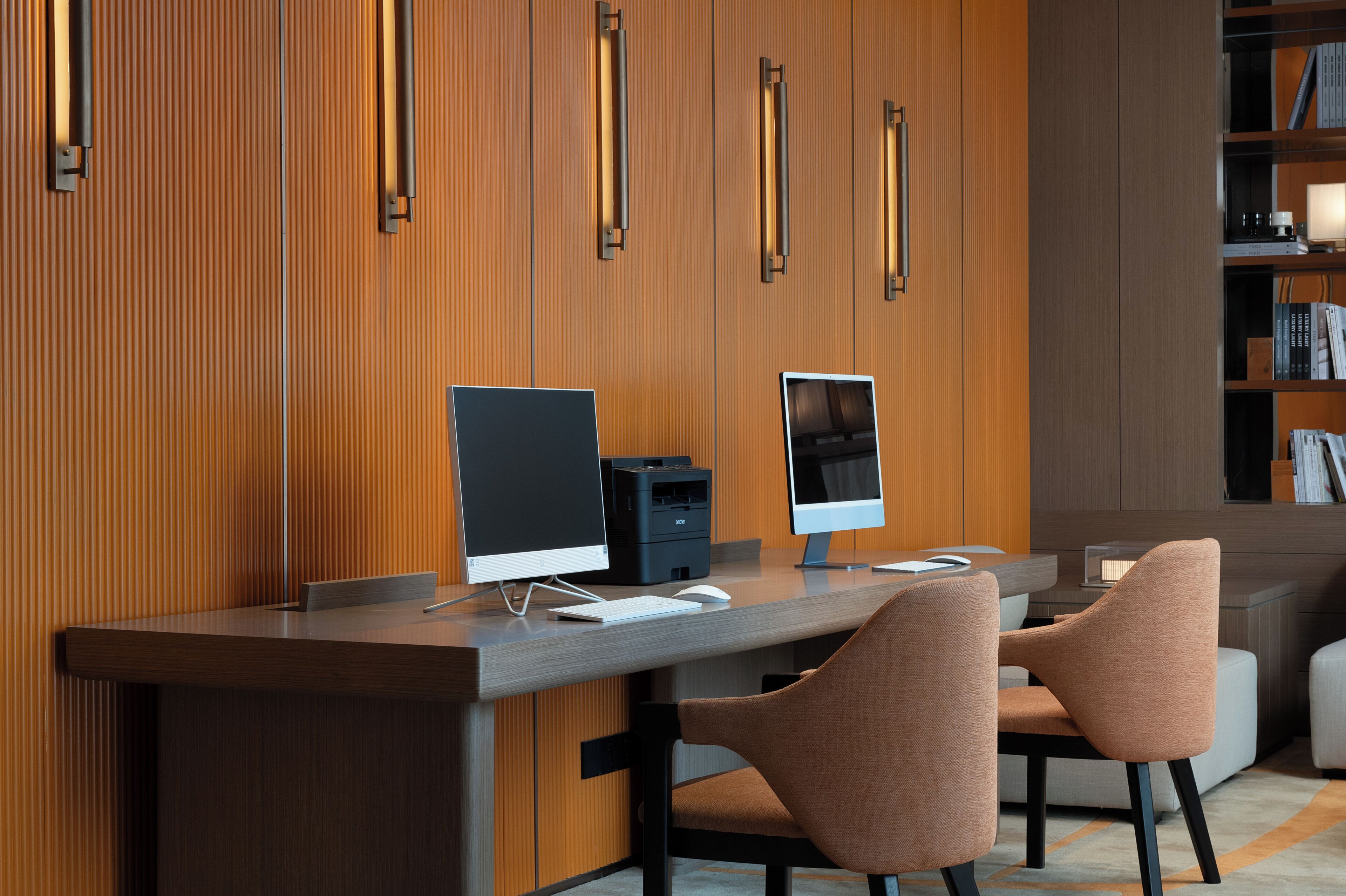 A modern office desk with two computers, a printer, and two chairs.