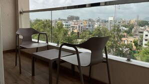Un balcón con dos sillas y una mesa, con vista a un paisaje urbano de edificios y árboles.