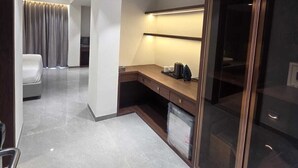 Una habitación de hotel moderna con piso de mármol, un escritorio de madera, un amplio armario y un área de baño separada.