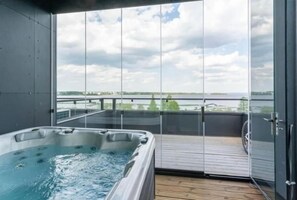 Un bain à remous sur un balcon, avec vue sur une étendue d’eau et un ciel nuageux.