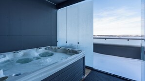Ein Whirlpool auf einem Balkon mit Blick auf ein Gewässer und einen klaren Himmel.