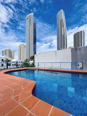 A swimming pool with a tiled deck, surrounded by high-rise buildings, under a clear sky. - Monte Carlo on  the  Coast (Surfers Paradise)