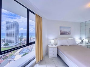 A hotel room with a large window, a bed, a bedside table, a lamp, and a painting on the wall. - Monte Carlo on  the  Coast (Surfers Paradise)