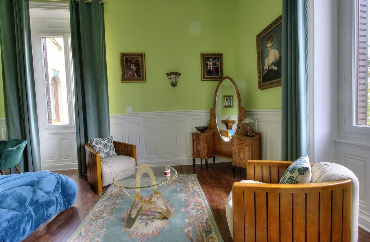A room with a green wall, a wooden chair, a blue sofa, a round coffee table, and a mirror.