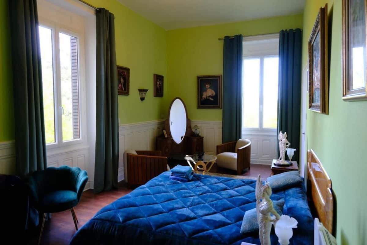 A bedroom with a large bed, a chair, a dresser, and a window with curtains.