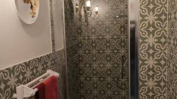 Une salle de bain avec une douche, des carreaux décoratifs, un porte-serviettes et une assiette décorative.