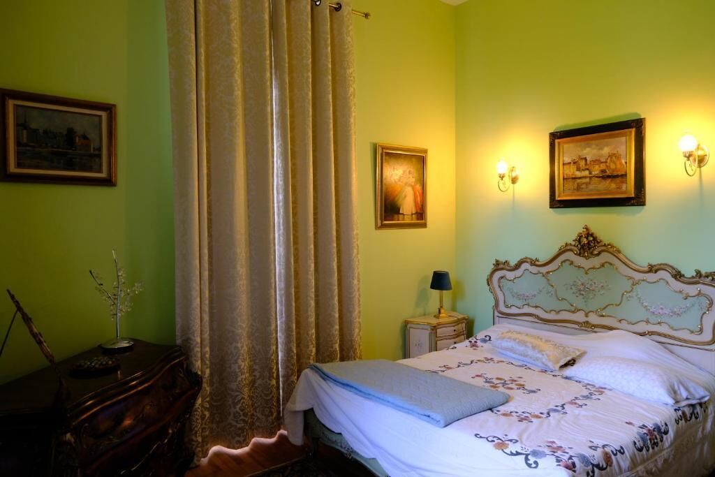 Un dormitorio con cama, cortinas, una mesita de noche, una lámpara y dos luces empotradas en la pared.