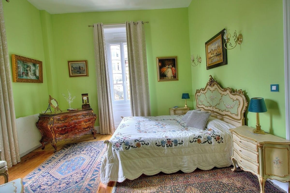A bedroom with a bed, dresser, nightstands, and a window with curtains.