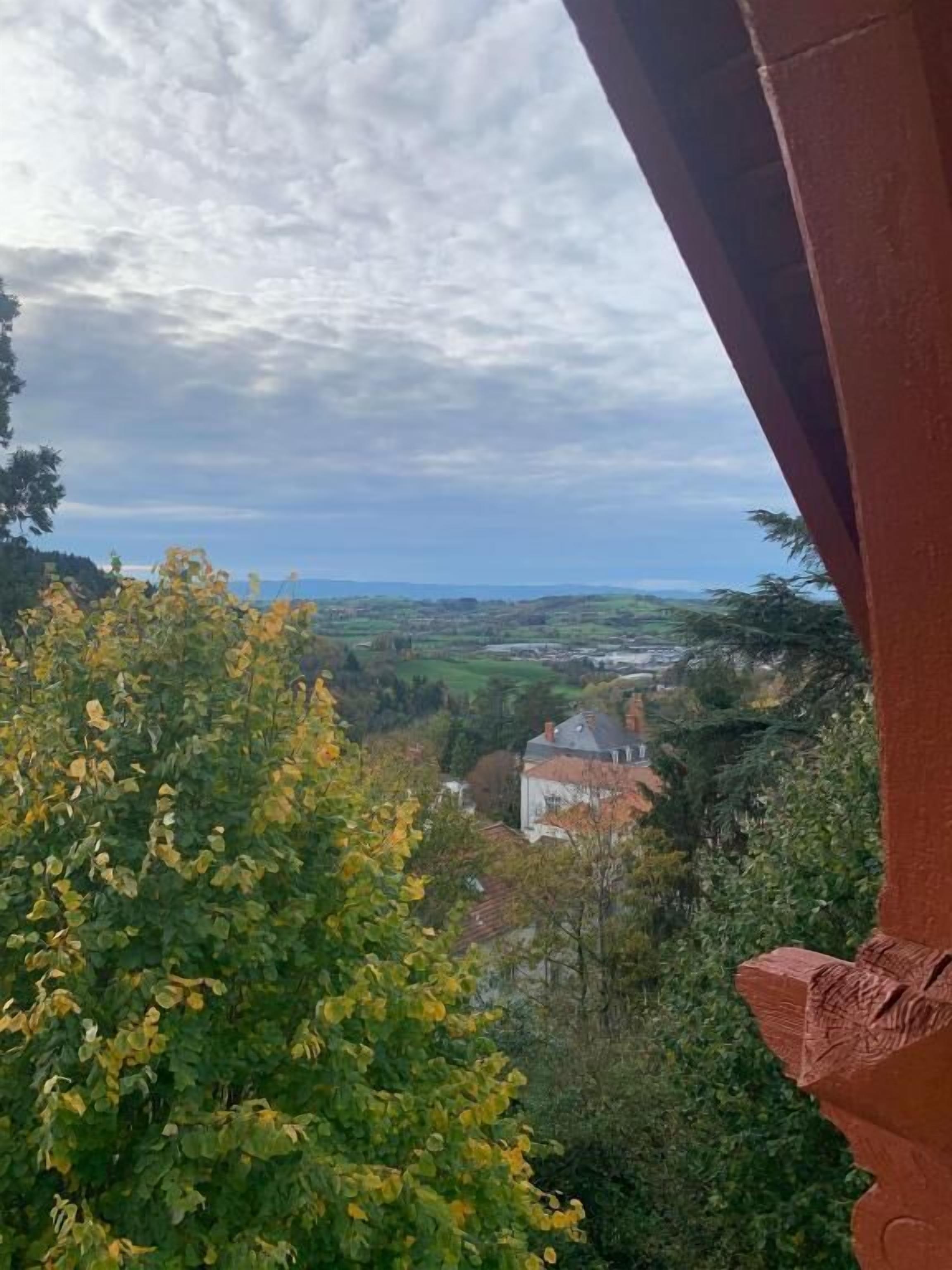 Uitzicht vanaf een balkon met een rode constructie, op een landschap met gebouwen en begroeiing.