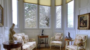 Una habitación con ventanal saliente, un sofá, una silla, una mesita y una estatua.