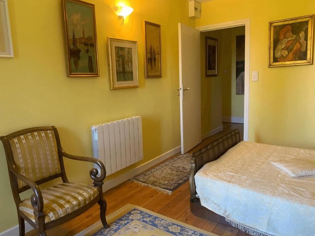 A bedroom with a bed, a chair, a radiator, and framed pictures on the wall.