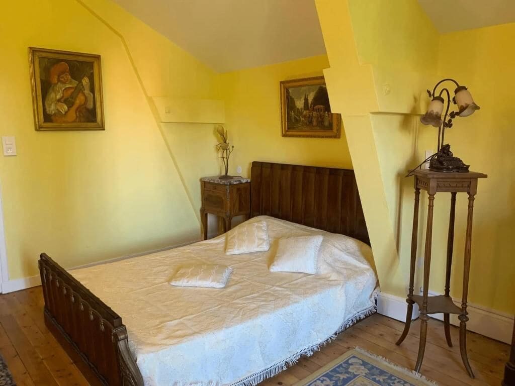 A bedroom with a wooden bed, a nightstand, a lamp, and two paintings on the wall.