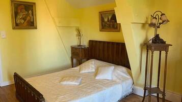 A bedroom with a wooden bed, a nightstand, a lamp, and two paintings on the wall.