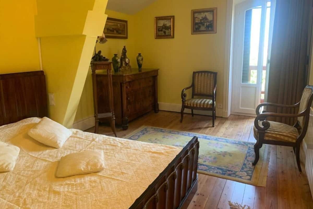 A bedroom with a bed, a dresser, a chair, and a door leading to a balcony.