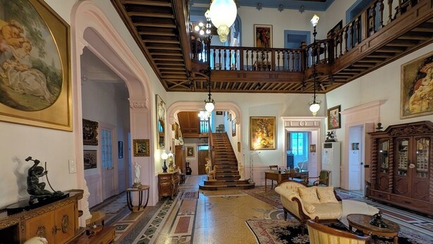 Un amplio vestíbulo con escalera, muebles ornamentados y un candelabro.