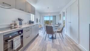 A modern kitchen with built-in appliances, a dining area with a table and chairs, and a view through a large window.