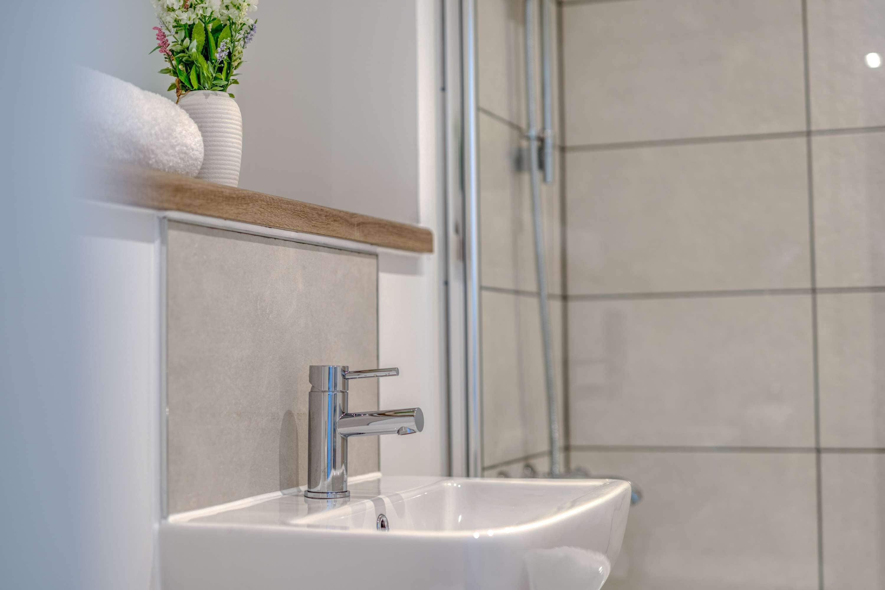 A bathroom with a white sink, a mirror, a towel, and a vase with flowers.