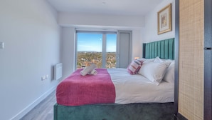 A modern hotel room with a large bed, a view of the city, and a green headboard.