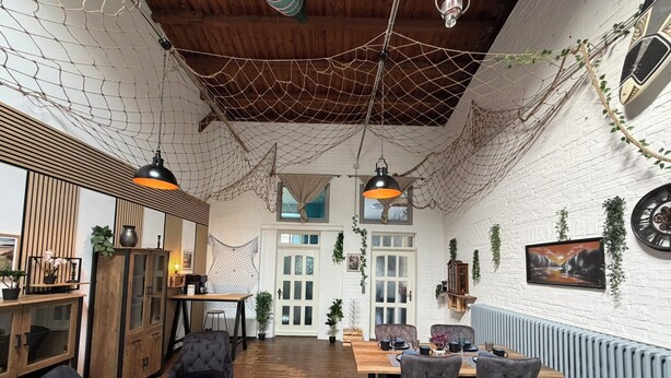 A cozy room with a wooden ceiling, a dining table with chairs, a sofa, and a cabinet with glass doors. - Wohnglück Alte Werft Leer (Leer (Ostfriesland))