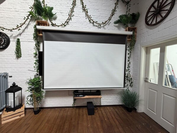 A room with a white brick wall, a white door, a wooden floor, and a projector screen.