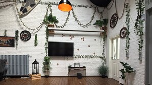 A room with a white brick wall, a mounted TV, wooden flooring, and various plants. - Wohnglück Alte Werft Leer (Leer (Ostfriesland))