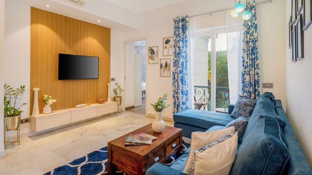 Ein modernes Wohnzimmer mit Flachbildfernseher, einer Wand in Holzoptik, einem blauen Sofa und einem Couchtisch.