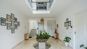 Ein geräumiger Flur mit einem zentralen Blumentopf, Stadtansichten in Bildern und einer Treppe zu einer oberen Ebene.
