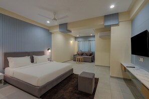 Quarto de hotel moderno com uma cama grande, um sofá, uma TV e um ventilador de teto.