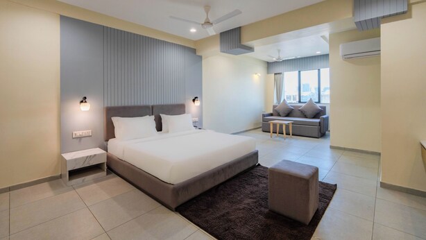 A modern bedroom with a large bed, a sofa, and a ceiling fan. - HOTEL MONVILLE ALKAPURI (Vadodara)