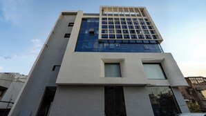 A modern building with a glass facade, multiple floors, and a flat roof. - HOTEL MONVILLE ALKAPURI (Vadodara)