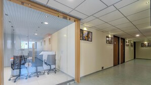 A hallway with glass walls, office chairs, and framed artwork on the walls. - HOTEL MONVILLE ALKAPURI (Vadodara)