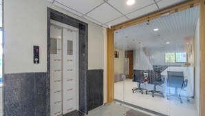 An elevator with a digital display, a glass partition, and office chairs in a modern interior. - HOTEL MONVILLE ALKAPURI (Vadodara)