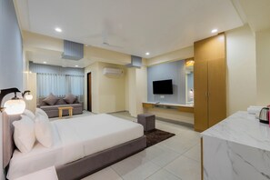 Quarto de hotel moderno com cama, sofá, televisão, secretária e casa de banho.