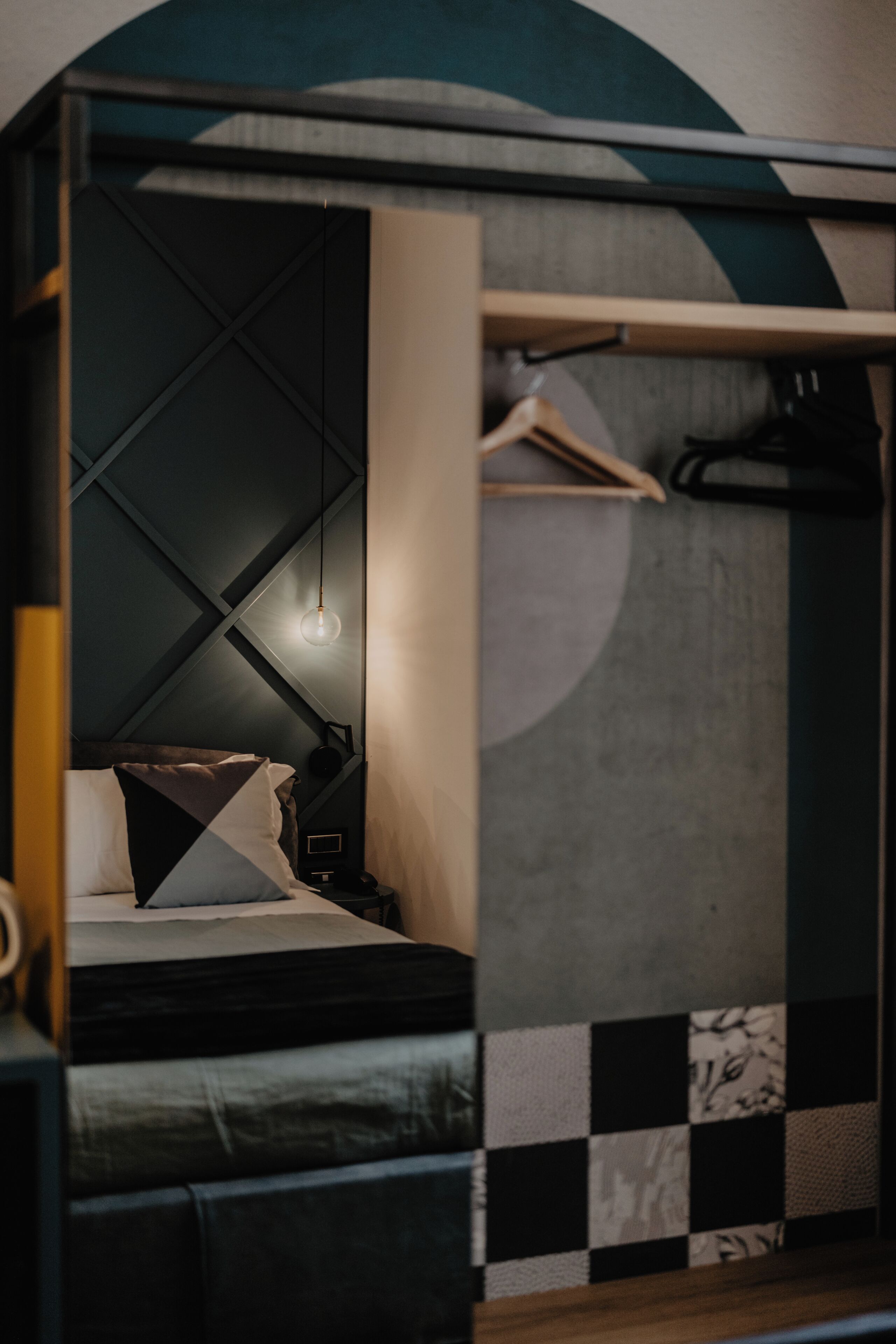 A modern bedroom with a geometric wall design, a hanging light fixture, and a bed with a geometric-patterned pillow.
