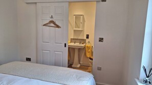 Ein Schlafzimmer mit einem Bett und einer Tür zu einem Badezimmer, das ein Waschbecken und einen Spiegel enthält.