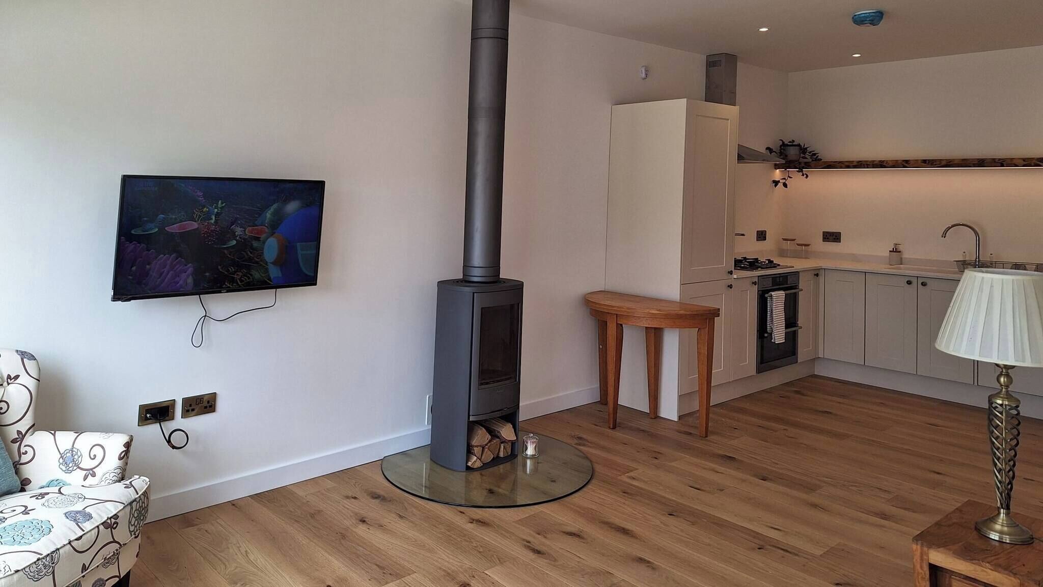 A modern kitchen with a built-in stove, a small dining area, and a TV mounted on the wall.