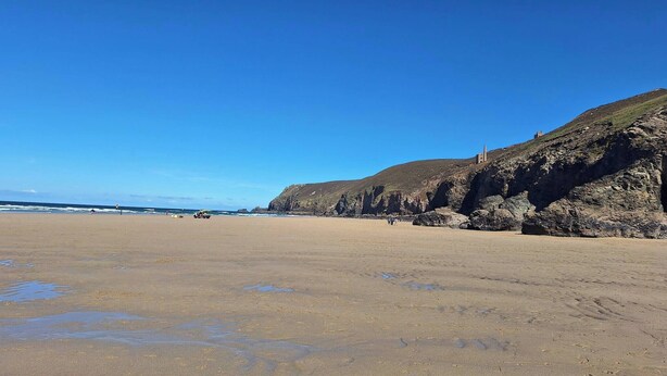 Ein weiter Sandstrand mit Felsküsten und einem klaren, blauen Himmel.
