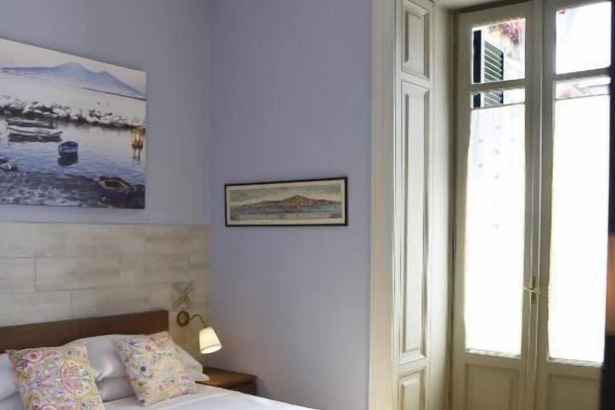 A bedroom with a bed, a nightstand, a lamp, a painting, and a door.