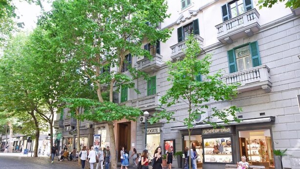 Una strada con pedoni, un edificio con un negozio chiamato 'SOMATERRA' e un altro negozio chiamato 'WOGUE'.