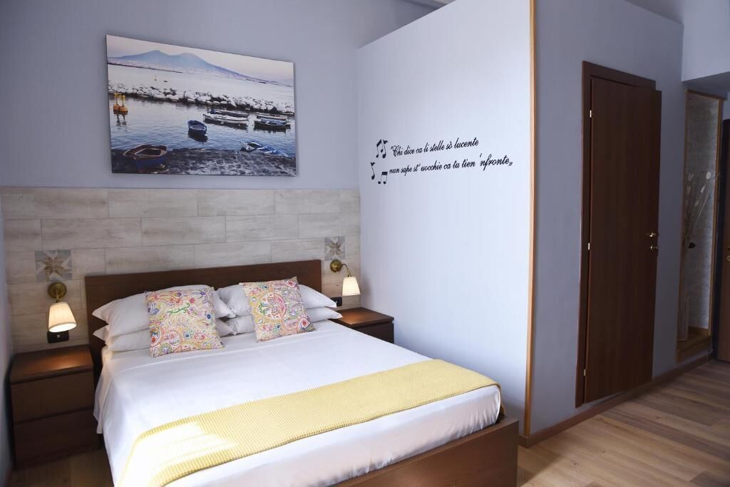A neatly made bed with a white comforter and decorative pillows, a wall-mounted artwork depicting a serene lakeside scene, and a decorative wall quote.