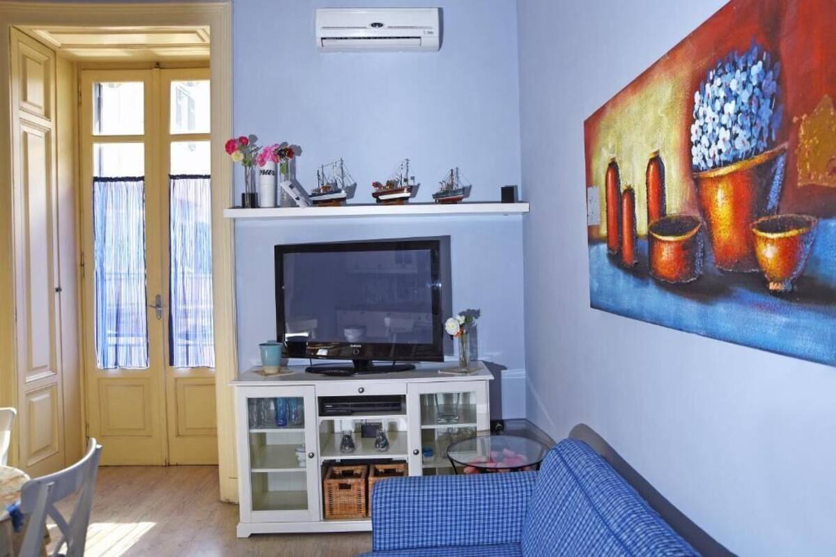 A living room with a television on a white cabinet, a painting on the wall, and a door leading to another room.