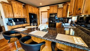A kitchen with wooden cabinets, granite countertops, and black bar stools.