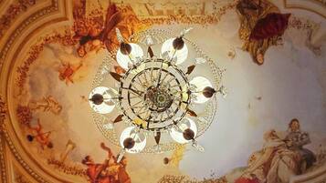 Un techo con una lámpara central y frescos que representan escenas históricas.