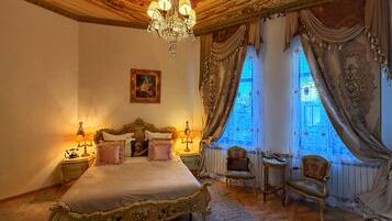 A luxurious bedroom with an ornate bed, a chandelier, and a view of a blue-tiled courtyard.