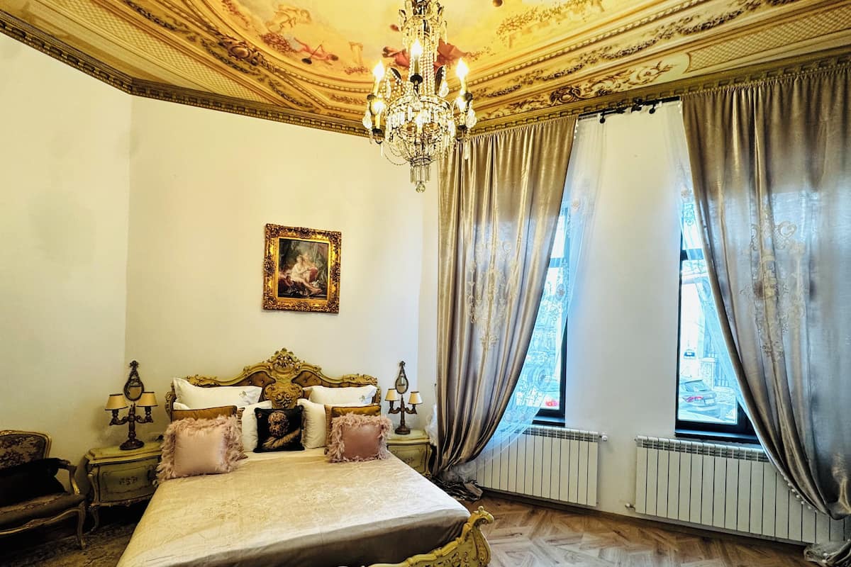 A bedroom with a large bed, ornate ceiling, and a window with curtains.