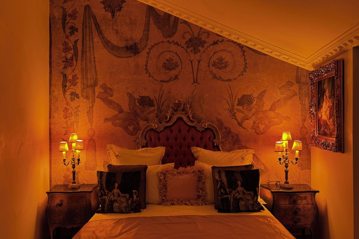 A bedroom with a large bed, ornate headboard, and decorative wall panels.