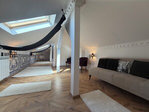 Un loft amplio con techo alto, tragaluces, un sofá grande, un sillón y una pared con diseño.