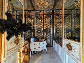 Un couloir orné de décorations raffinées, une commode blanche à tiroirs et une grande plante noire aux feuilles plumeuses.