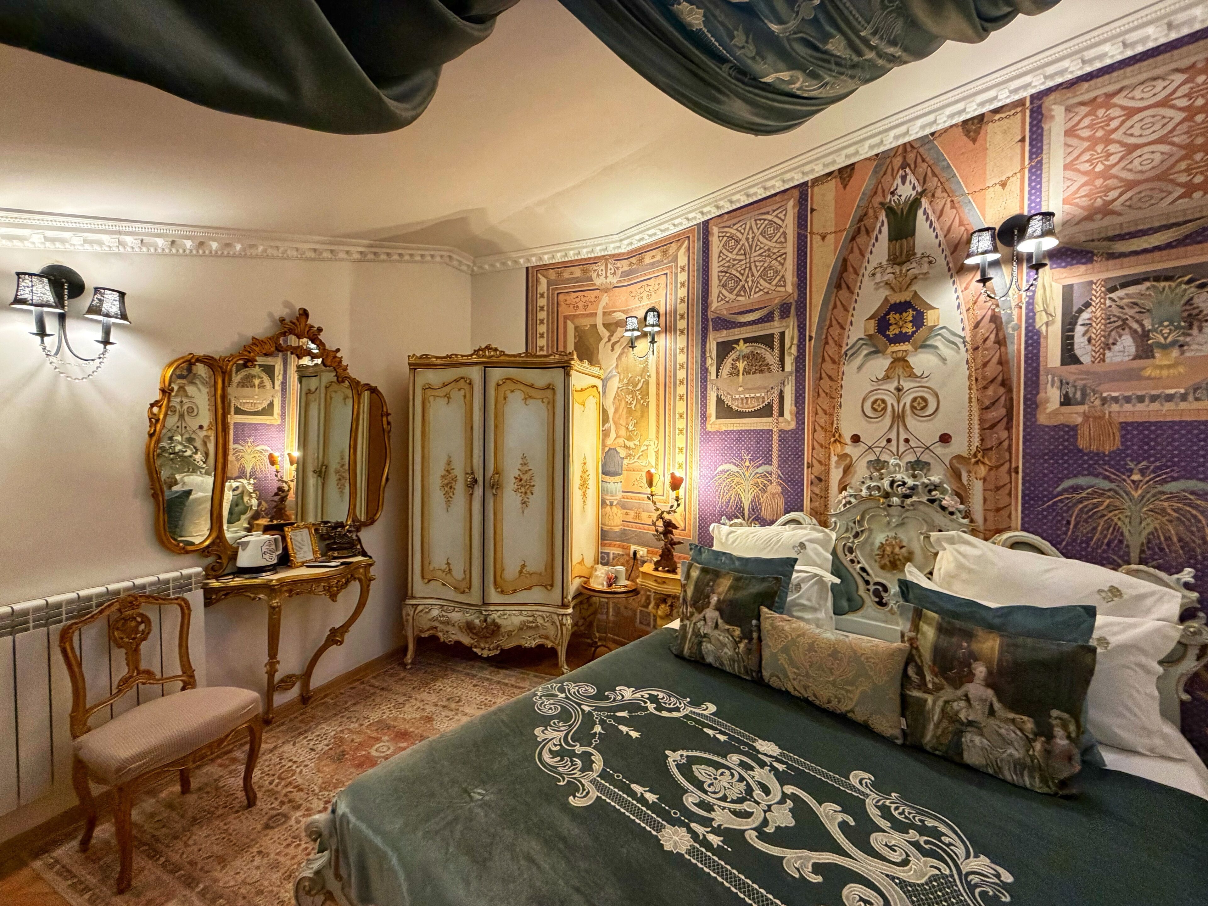 A room with a bed, a chair, a mirror, a wardrobe, and a wall with decorative patterns.